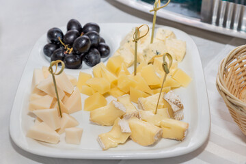 Cheese plate on a white table. Many kinds of cheese on a plate withred grape served