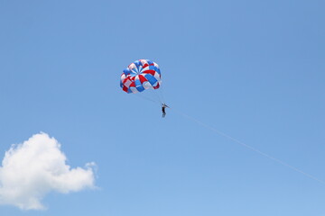 Fototapeta na wymiar A woman is gliding using a parachute on the background of cloudy blue sky.