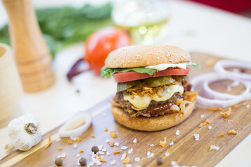 Homemade burger with beef, fried bacon and onion on wooden cutting board