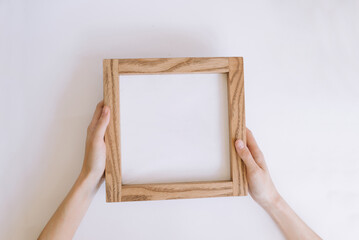 Wooden frame in female hands with place for inscription or photo. mock-up with a wooden frame on a white background
