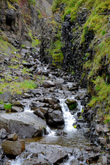 Bach fliesst einen Berghang hinab in das Tal Heydalur