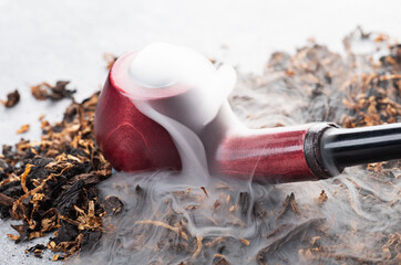 A wooden smoking pipe with smoke lies on tobacco on a light background. close-up.