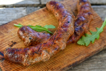 Fototapeta premium Grilled pork juicy sausages on wooden board outdoors. Grilling food, bbq, barbecue, picnic