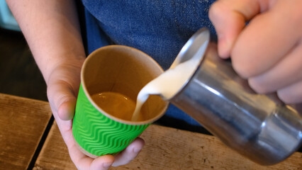 barista makes cappuccino in a ceramic mug pours milk into coffee
