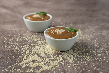 two white bowls with tahin and sesame on it and on the table, focus on foreground