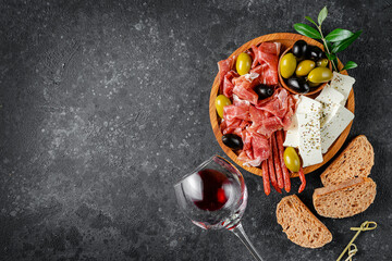 Appetizer wooden plate with meat, cheese and olives on dark concrete background. Copy space, flat lay.