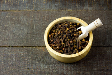 Cloves in wooden bowl with scoop on rustic wooden background. Herbal cloves have a fragrant and...