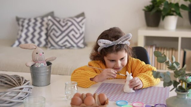 Portrait of an adorable little girl painting an Easter bunny ornament made of mud. Home crafts to decorate for easter day.
