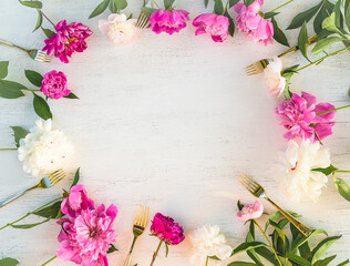 Frame of white and pink peonies with leaves, golden forks on white wooden background; Holiday background
