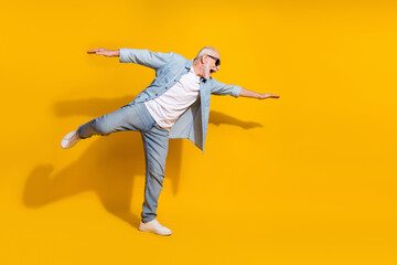 Fototapeta na wymiar Full length body size view of attractive cheerful motivated grey-haired man having fun flying isolated on bright yellow color background