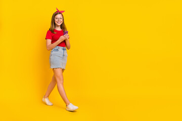 Fototapeta na wymiar Full size photo of adorable charming little kid girl go on walk with phone little teen influencer isolated on yellow color background