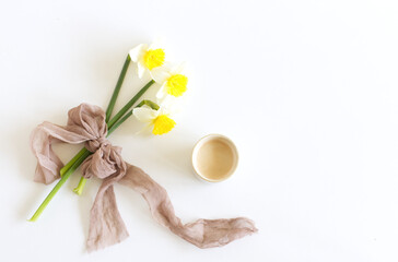 Fototapeta na wymiar Spring wedding still life. Silk ribbon, narcissus daffodil flowers on a white. Cup of coffee with milk. Breakfast composition, Easter.
