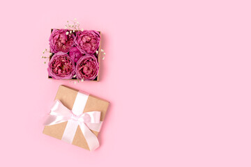 Open gift box with rose flowers inside. Festive concept on a pink background with copyspace.