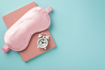 Top view photo of the pink sleeping mask notebook under it and white little clock on the notebook isolated in a light blue background copyspace