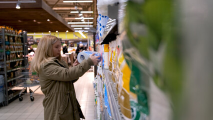 blonde woman picks up goods in the housekeeping department of a supermarket