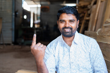 Happy indian carpainter or craftman showing ink marked finger by looking at camera after voting on...