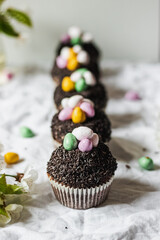 Homemade Easter chocolate cupcakes with chocolate butter cream frosting and candy eggs. Easter brunch. spring blossom decoration. on white linen tableclouth Happy easter day. Easter recipes.
