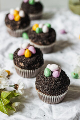 Homemade Easter chocolate cupcakes with chocolate butter cream frosting and candy eggs. Easter brunch. spring blossom decoration. on white linen tableclouth Happy easter day. Easter recipes.