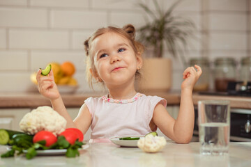A happy girl 2-3 years old in the kitchen at home or in kindergarten eats delicious and healthy vegetables for lunch.