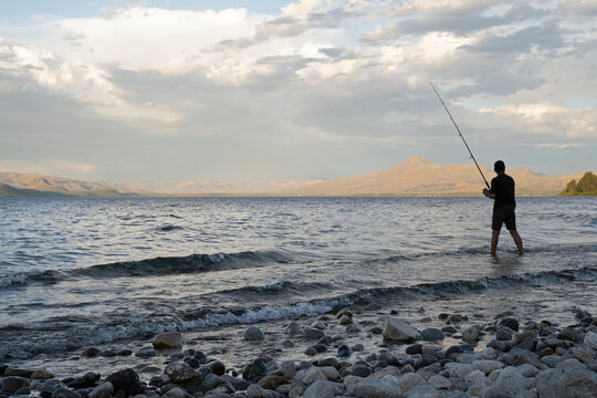Sports and recreation. View of a man fishing from the rocky shore in Nahuel Huapi lake at sunset. 