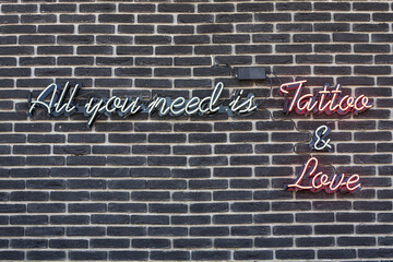 Fototapeta premium Neon sign All you need is Tatoo and love on the wall of a stone house