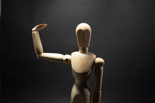 The wooden mannequin raising arm and greets. on a black background
