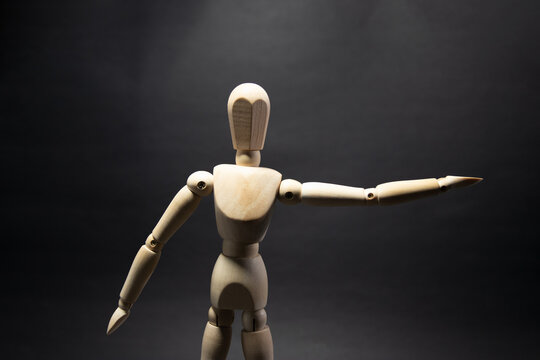 The wooden mannequin stopping something with his left hand on a black background