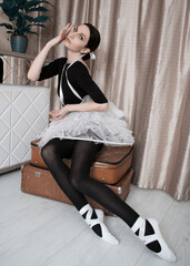 Beautiful brunette ballerina in a tutu skirt and pointe shoes posing while sitting on retro...