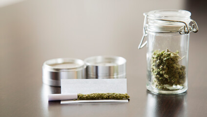 marijuana cigarette with metal grinder and airtight container, on brown table