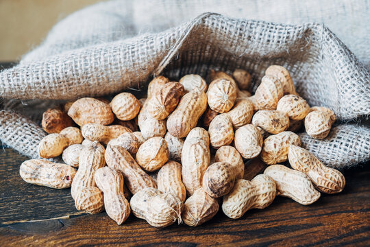 Roasted Peanuts In Shell Poured Out Of Bag On Wooden Table. For Making Healthy Sweets, Sandwich Sauce, Pasta.