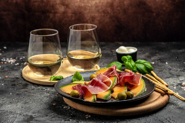 Cantaloupe melon with prosciutto or jamon and green basil leaves with glass of wine. delicious superfood salad, Traditional Italian snack antipasti. place for text
