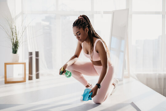 Millennial African American woman in sportswear wiping yoga mat after training at home gym, empty space