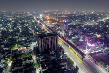 aerial drone shot with elevated metro train tracks over busy street with light trails from traffic skyscrapers on side in hyerabad jaipur india
