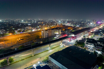 Fototapeta na wymiar aerial drone shot showing elevated metro train station and tracks over busy street with light trails from traffic and cityscape in gurgaon, jaipur India