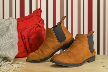A pair of tan brown Chelsea boots and a hand bag on wooden floor. Fashion and style concept.