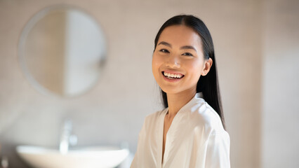 Cheerful pretty chinese lady smiling at camera, bathroom interior