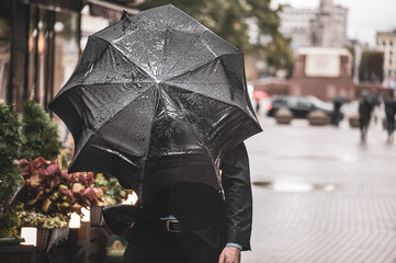 A man with a black wet umbrella was caught in a gust of wind on the street of the old city.