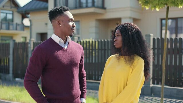 Cinematic close up portrait on beautiful african american man and woman standing near fense. Looking serious into each other and smiling in camera. Couple enjoying warmth and sunlight.