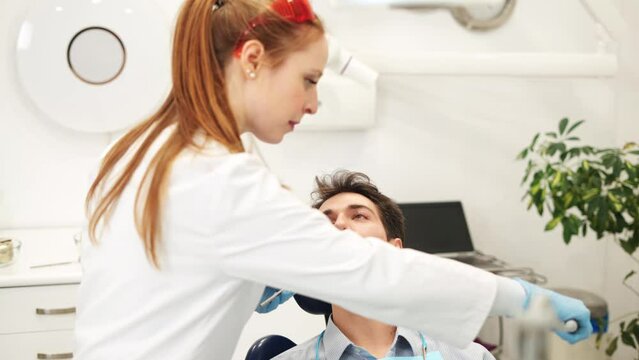 Young female dentist examining teeth of male patient with mouth mirror during check-up