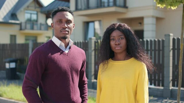 Cinematic close up portrait on beautiful african american man and woman standing near fense. Looking serious into each other and in camera. Couple enjoying warmth and sunlight.