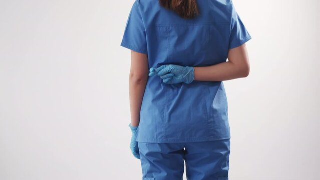 Fake medicine. Medical luck. Health care fraud. Back view of woman doctor showing crossed fingers in lie gesture isolated on white background.
