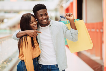 Portrait of black couple with shopping bags pointing at window