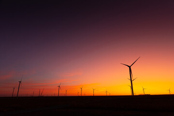 Obraz premium Sunset over an eolian wind farm with amazing sky color. Alternative eco energy good for the environment. Renewable energy industry.