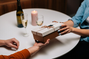 Close-up high-angle view of man giving wrapped box with gift to woman at table with candles on birthday or Valentines Day. Happy wife receiving present from husband enjoying romantic dinner date.