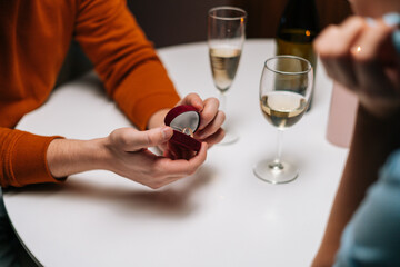 Close-up hands of unrecognizable loving young man making proposal for marriage to woman at table with candles, marry me. Beautiful romantic couple having dinner celebrating Valentines day in dark room