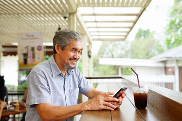 asian senior man using smartphone while drinking in cafe outdoor, concept elderly people using social network technology