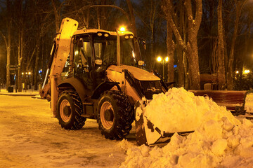 cleaning snow in the park in winter with a tractor in the evening