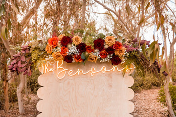 Wood wedding backdrop neon sign reads The Bensons fall floral decorations