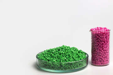 Green and pink granules of polypropylene or polyamide on a white background. Plastics and polymers industry. Copy space. Glass petri dish, flask, volumetric glassware, test tube.