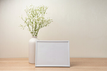Portrait white picture frame mockup on wooden table. Modern ceramic vase with gypsophila.Scandinavian interior